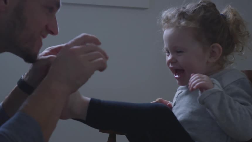 A man playing with a baby girl in a rocking chair