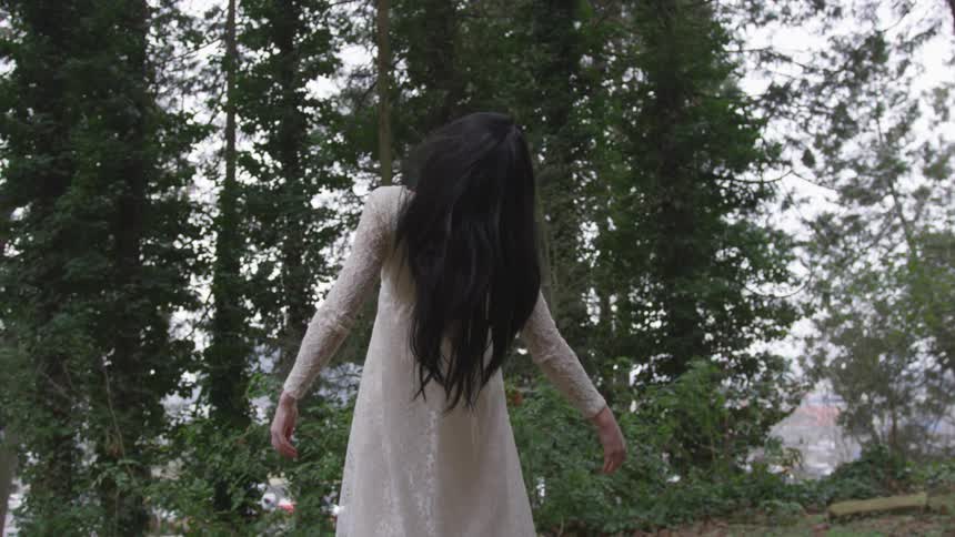 A brunette haired woman in a white dress stretching in a forest