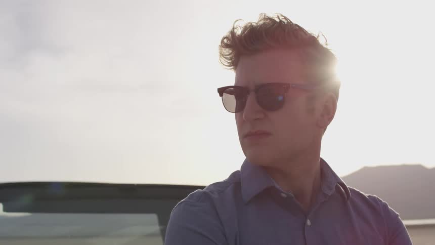 Man stands by vehicle wearing shades and looking around