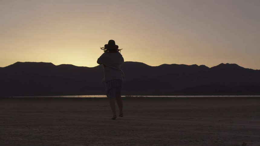 Woman spins on arid plain as sun sets behind rocky ridge