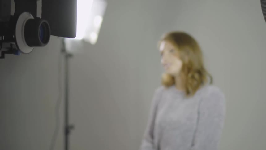 A girl sitting on a yellow stool is talking under the bright lights as the camera moves around her
