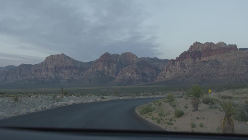 Car slows drives down a road of a nearly barren landscape full of mountains with geographical layer lines after the sun has set
