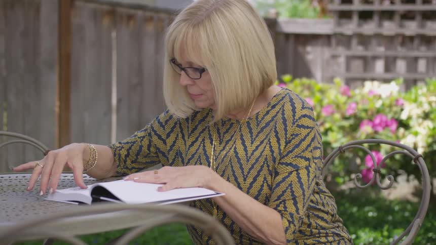 A woman reading a book at a table in the garden