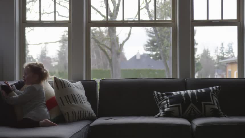 A young girl runs and jumps on a living room sofa