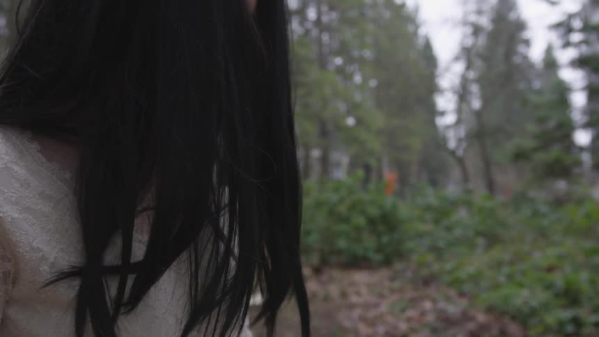 A child with dark hair covering the face is alone in the woods