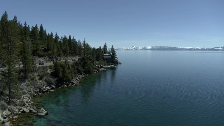 Roadway next to a large forest and mountain lined lake