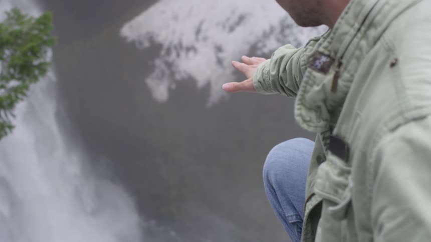 Man reaches out from a cliff to the waterfall below