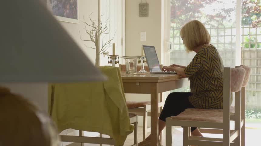 Woman sits at a table and types on her laptop