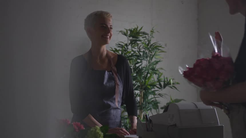 A woman is selling flowers to a man in her shop