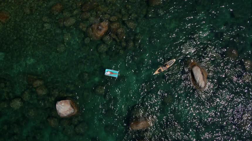 A boat floats along the water next to a lounging woman