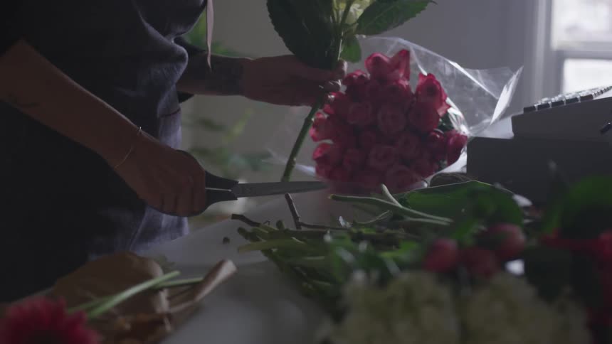 A florist trims a flower stem next to a cash register