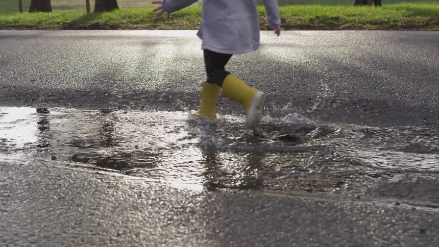 Child wearing galoshes splashes through puddle on street