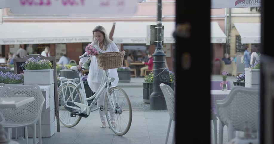 A woman parks her bike by restaurant tables outside
