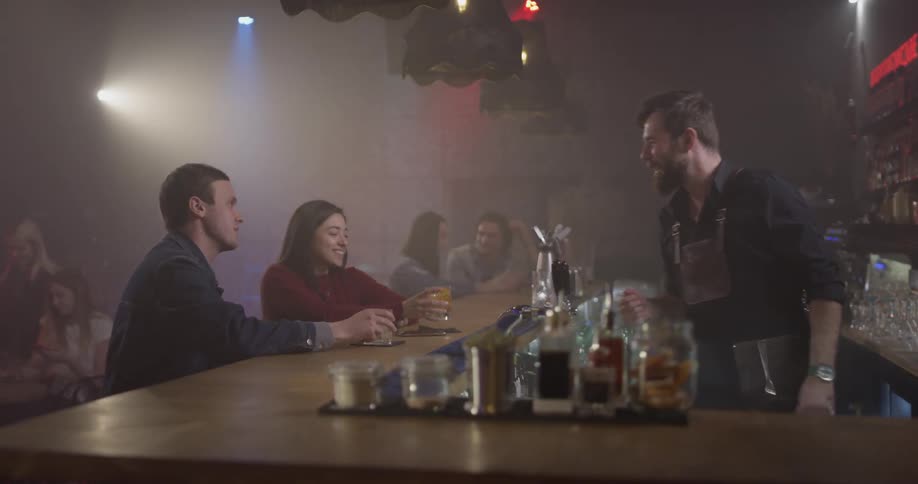 People sitting at a bar, and two of them toast each other