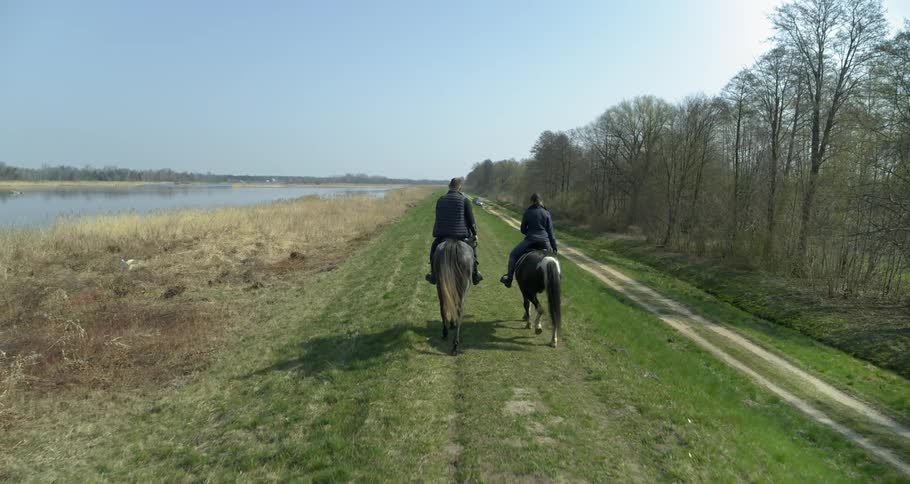 Two people riding horseback in a field along a river