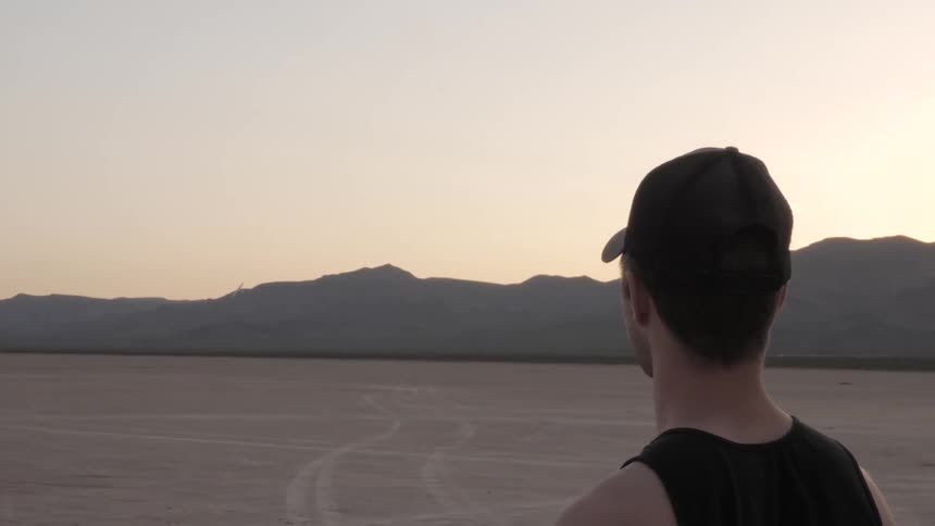 Man looks at the distant drone in the desert at sunset