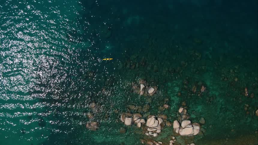 Canoe floats in sparkly water near rocks