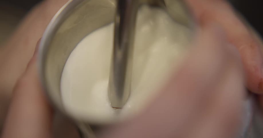 Milk is frothed in a metal cup with a stick blender