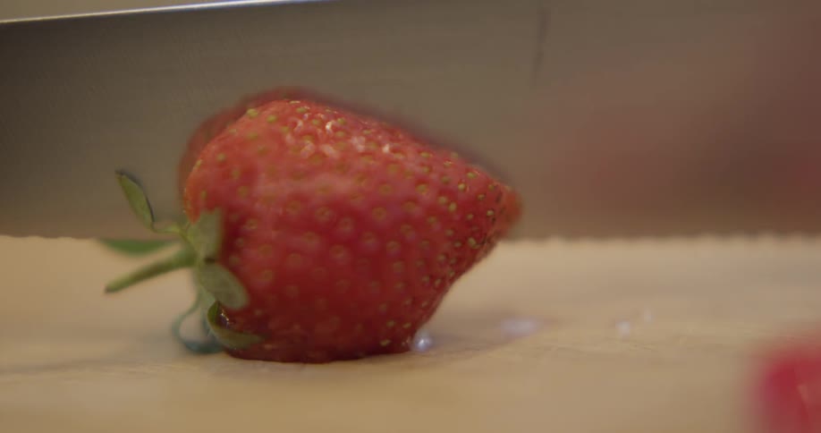 A knife slices through a strawberry