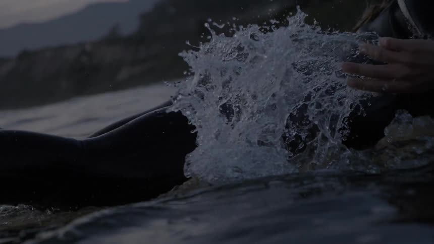 Female surfer paddles surfboard towards land