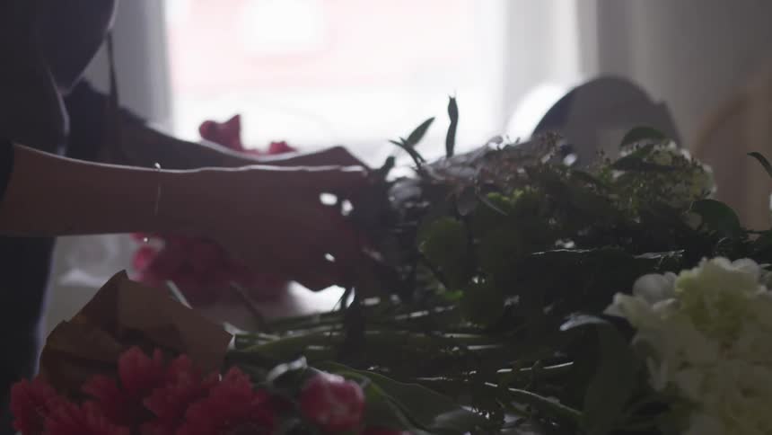 A florist picks up a bunch of flowers next to a cash register