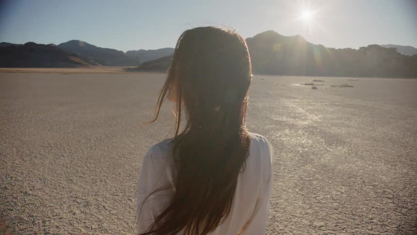 A long-haired woman walking and looking around in a desert