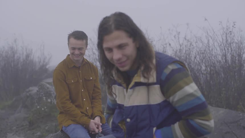 Two men wearing coats sit on a rock