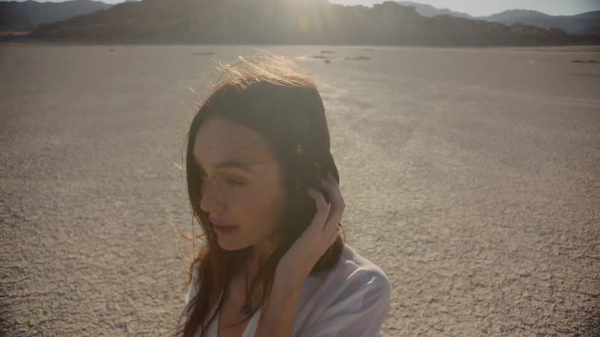 A woman standing on a dry lake bed in a white dress