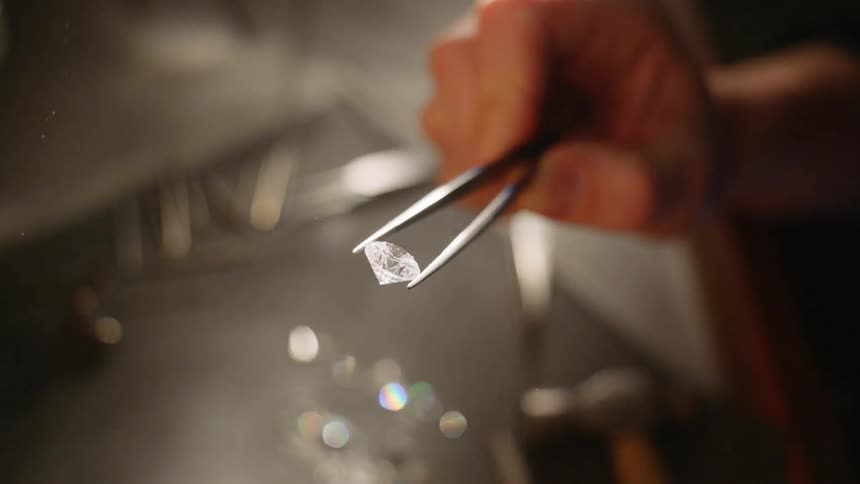A person holds a small diamond with tweezers indoors