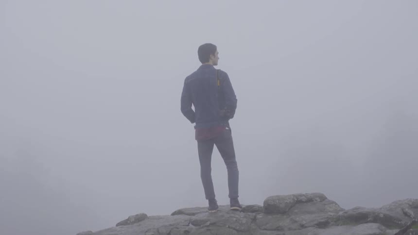 Man looks off a foggy cliff into the distance
