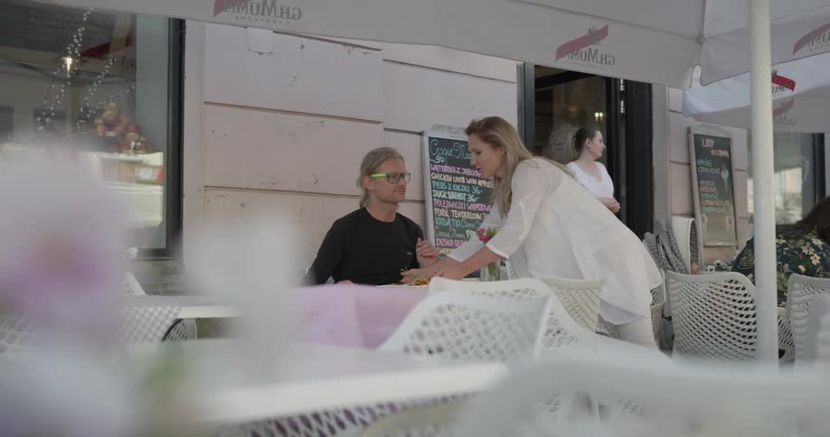 A waitress places utensils and a plate of food on a table in front of a man