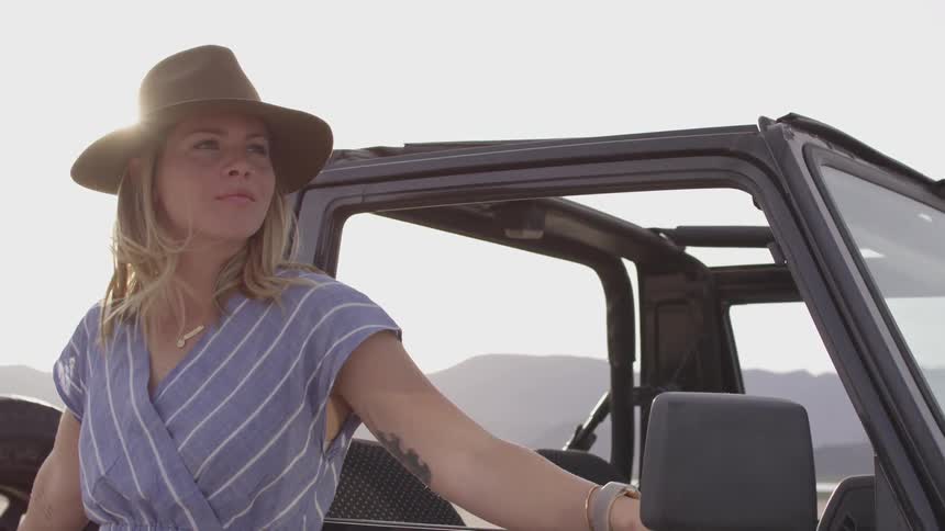 A woman in a hat stands beside a vehicle