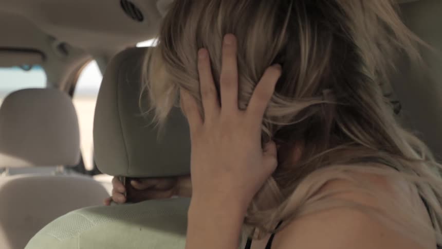Woman's hair flaps in the wind as she sits in the backseat of a car with open windows