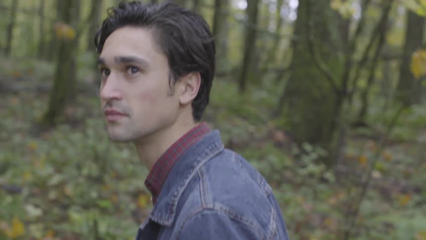 A young man looks around as he walks through a forest