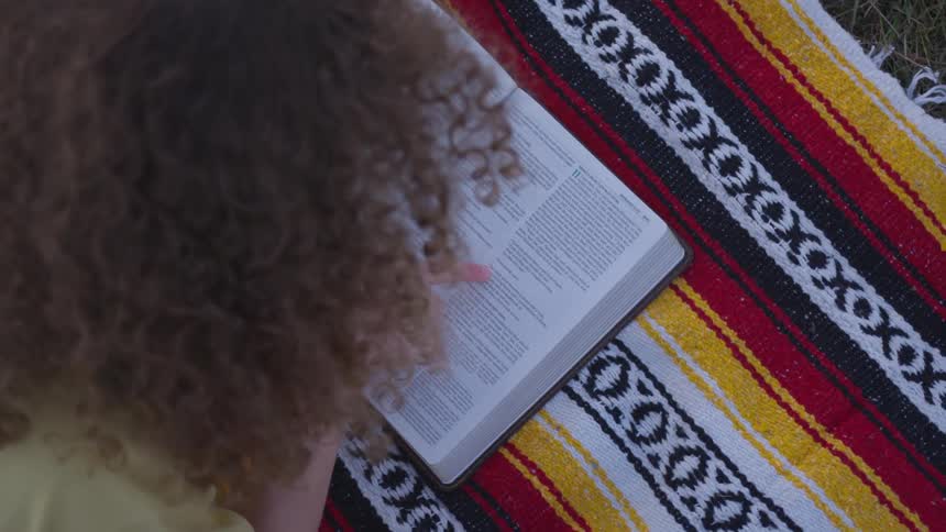 A woman reading a book outdoors on a blanket