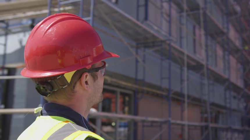 Man in red hard hat surveys building under construction
