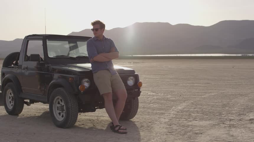 A man standing in front of a car on a dry lake bed