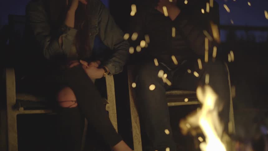 Two people sit by a campfire