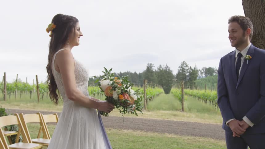A woman in a wedding dress carrying flowers to a man