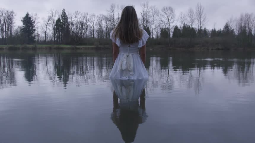 Woman in dress stands submerged in a lake