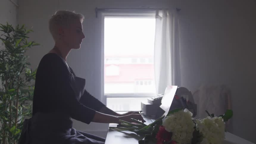 Woman types on a computer on a table with a bouquet of flowers on it