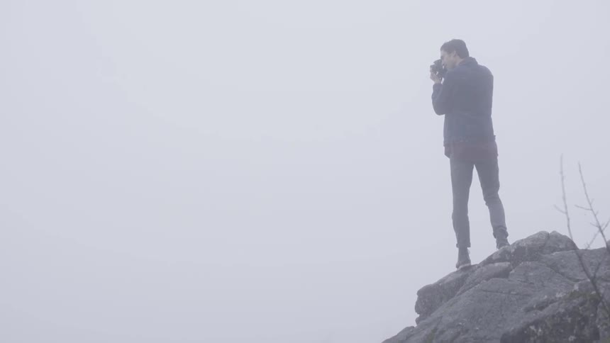 A man stands on a cliff edge and takes a picture