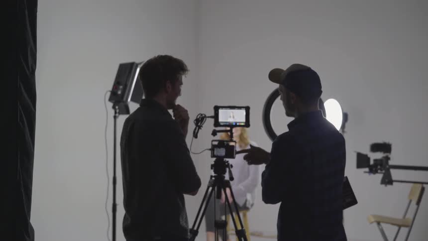 Two men talking in front of a camera on tripod in a studio