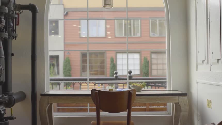 Chair sits at desk in front of a bare window as person walks by outdoors
