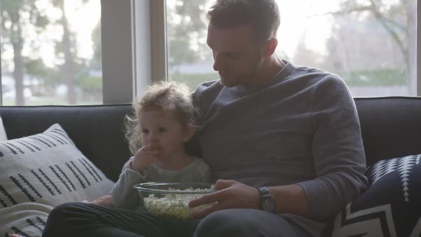 A man and his daughter eating popcorn on the couch
