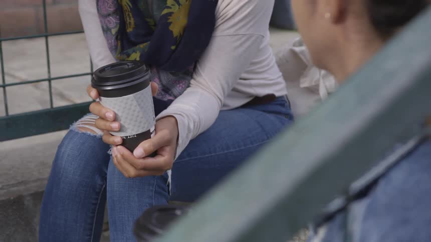 Two women sit and have a chat with plastic coffee cups