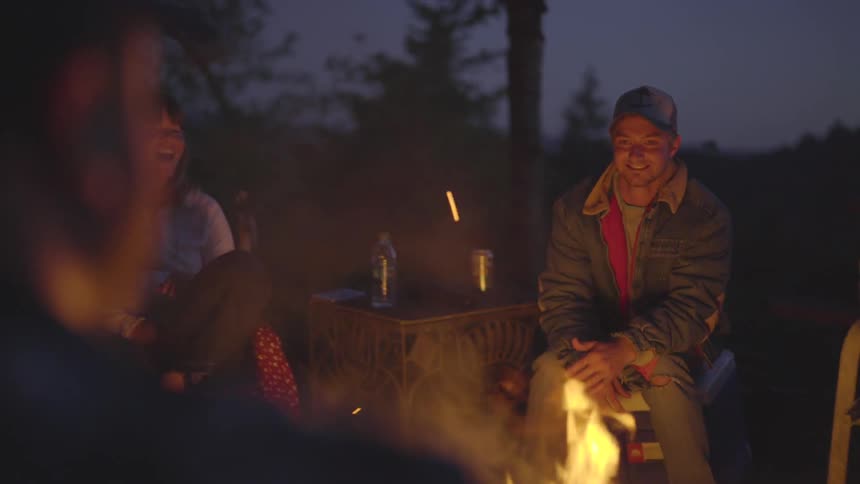 People talk and laugh around campfire at night