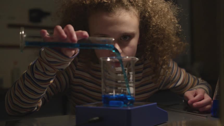 A girl fills a beaker with blue liquid from a test tube