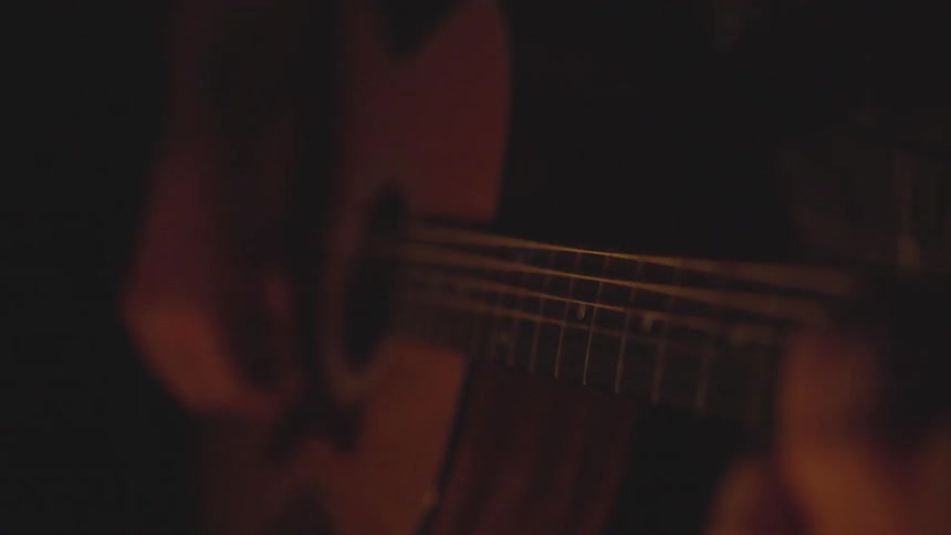 A man sits by a fire and strums a guitar