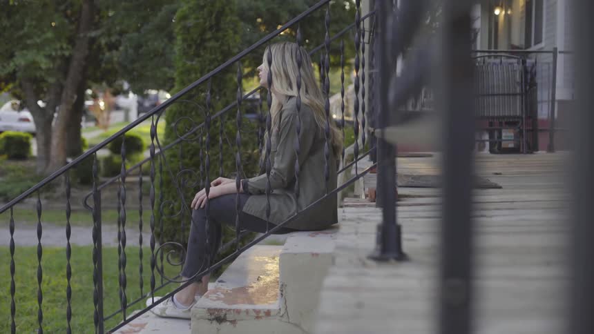 Woman sitting on a front porch next to green grass and shrubs